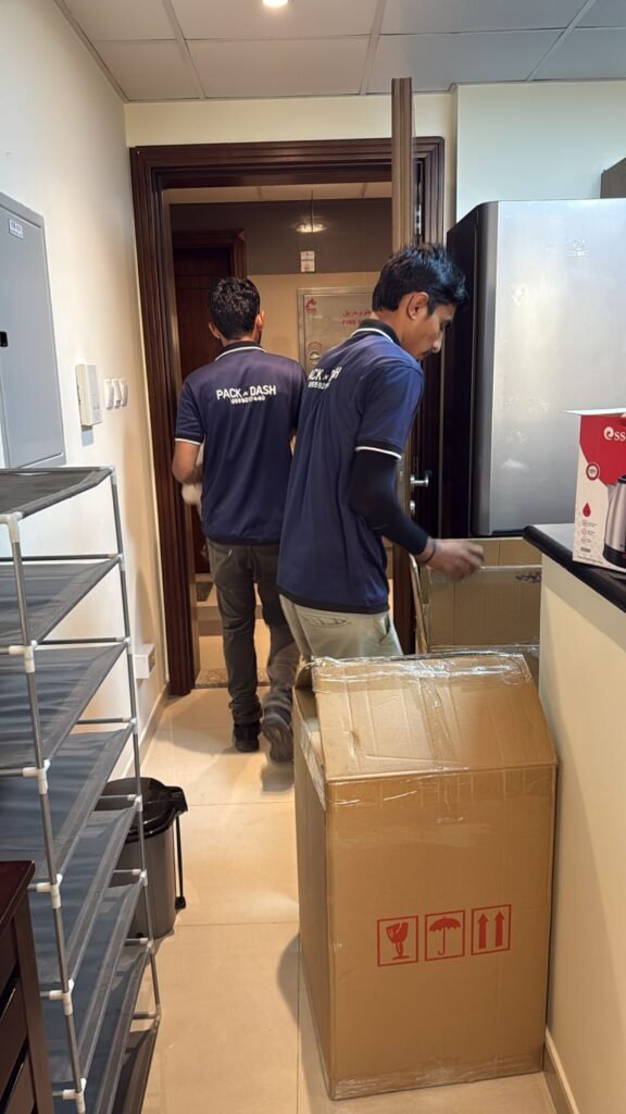 Two PacknDash movers carrying a packed box out of a Dubai apartment doorway